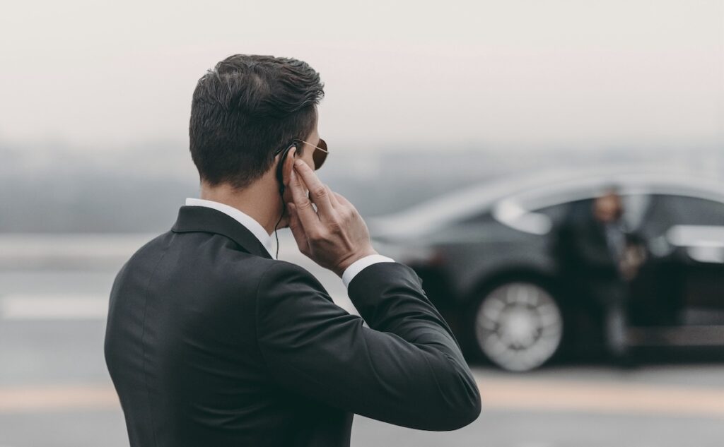 Mann im Personenschutz blickt auf Fahrzeug mit Schutzperson